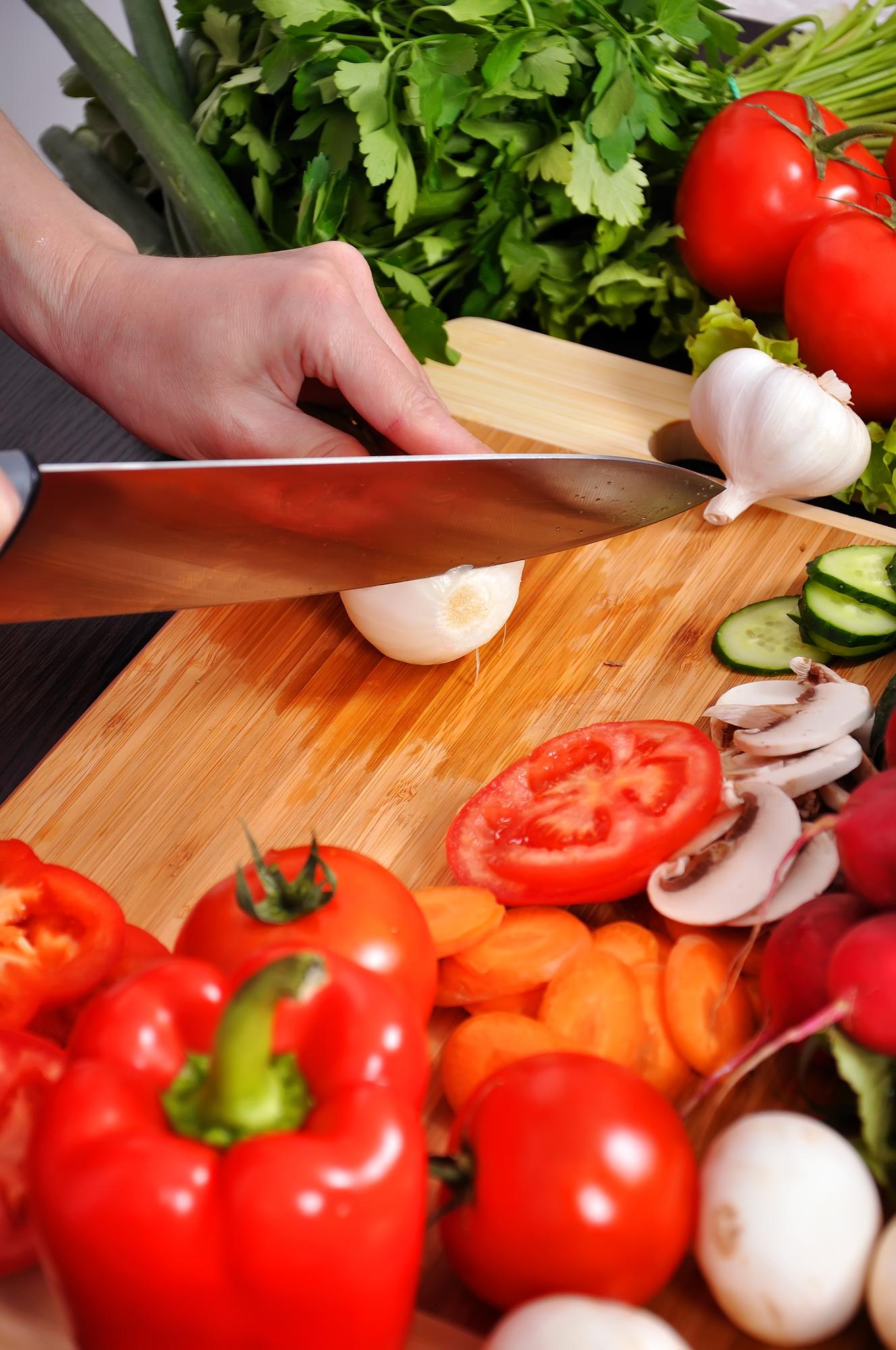 Detalle de manos cortando ingredientes frescos en tabla de madera